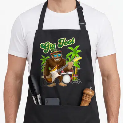 Tablier de cuisine noir avec illustration d'un Bigfoot Rasta jouant de la guitare électrique devant des palmiers et un set de batterie.