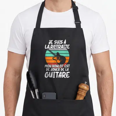 Tablier de cuisine noir avec une silhouette de guitare et le texte Je suis à la retraite mon boulot est de jouer de la guitare en blanc.