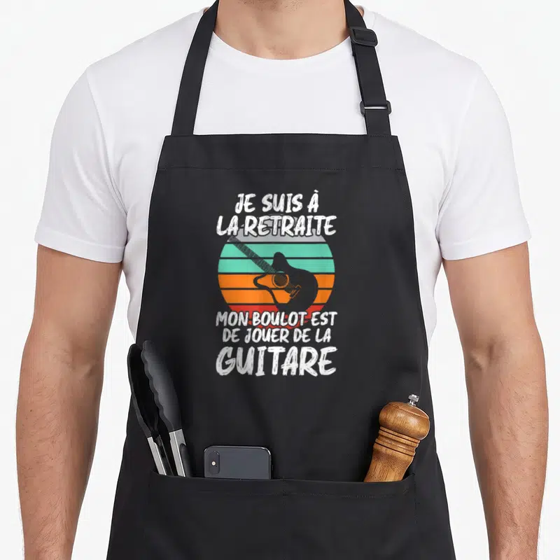Tablier de cuisine noir avec une silhouette de guitare et le texte Je suis à la retraite mon boulot est de jouer de la guitare en blanc.