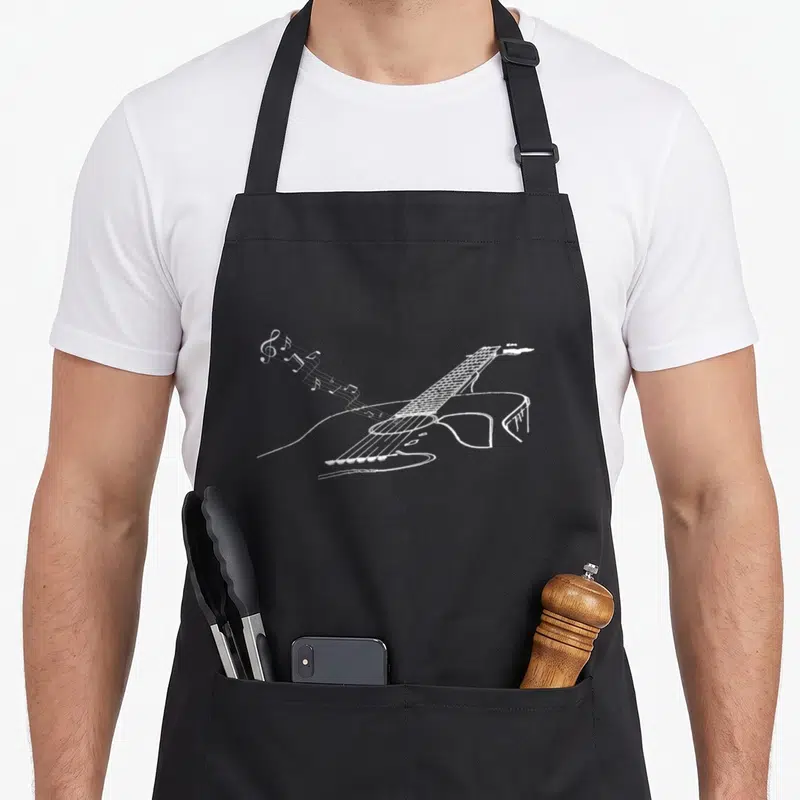 Tablier de cuisine noir avec illustration blanche d'une guitare acoustique et de notes de musique volantes.