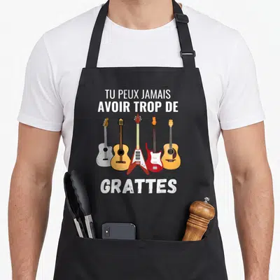 Tablier de cuisine noir avec cinq guitares et le texte Tu peux jamais avoir trop de grattes imprimé en blanc.