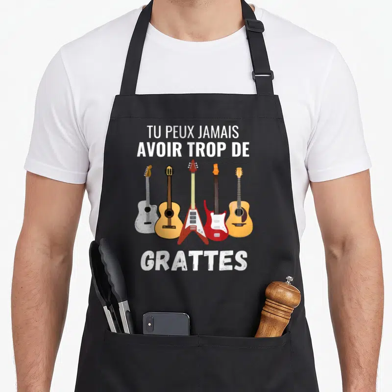 Tablier de cuisine noir avec cinq guitares et le texte Tu peux jamais avoir trop de grattes imprimé en blanc.