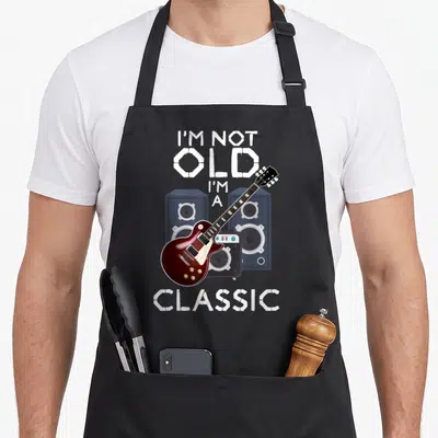 Tablier de cuisine noir avec une guitare électrique rouge, des enceintes et le texte I'm Not Old I'm A Classic en blanc.