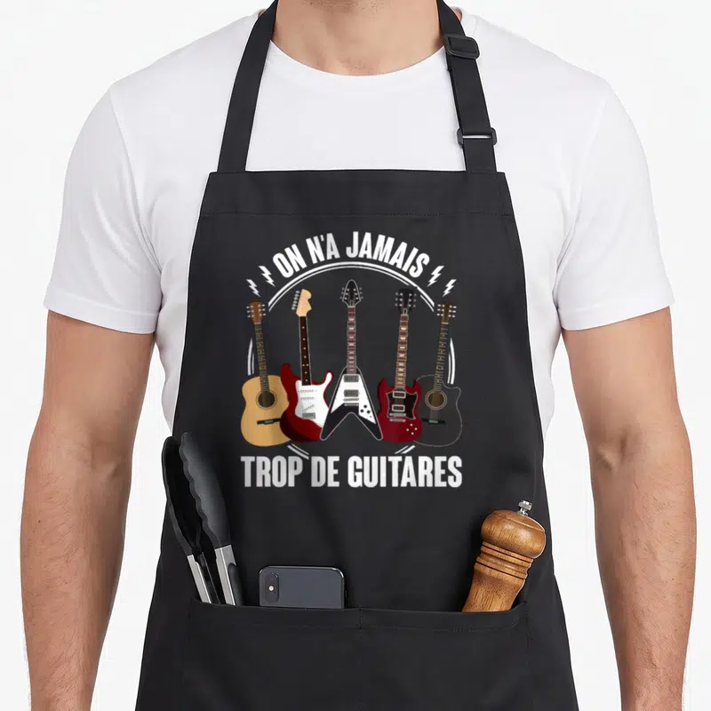 Tablier de cuisine noir avec cinq guitares illustrées et le texte on n'a jamais trop de guitares en blanc.