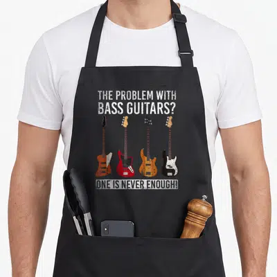 Tablier de cuisine noir avec quatre illustrations de basses électriques et un texte humoristique en anglais blanc.