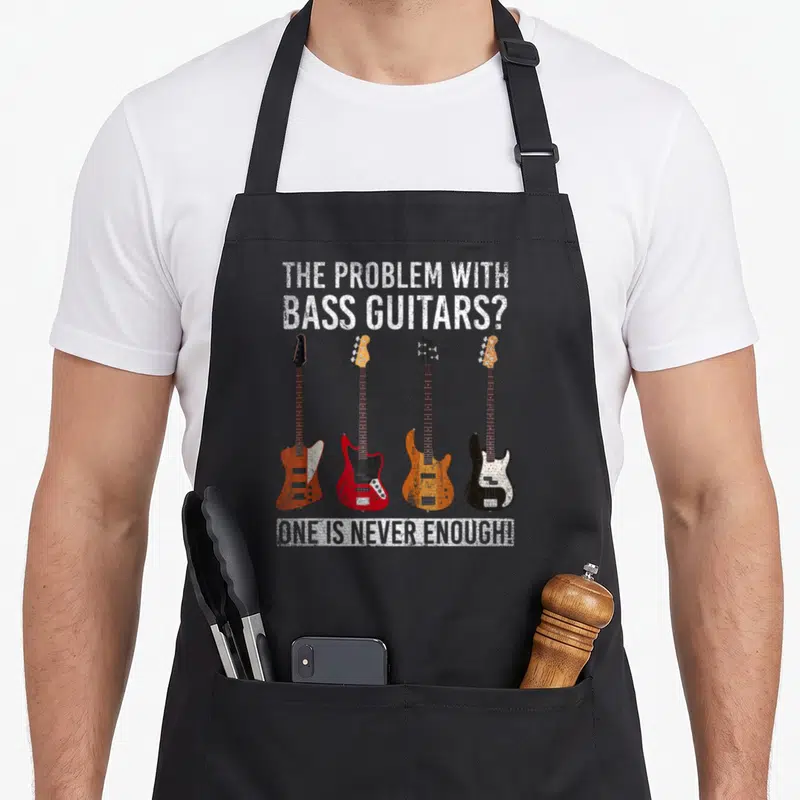 Tablier de cuisine noir avec quatre illustrations de basses électriques et un texte humoristique en anglais blanc.