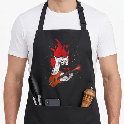 Tablier de cuisine noir avec illustration d'un chat blanc jouant d'une basse orange aux cheveux en feu rouge.