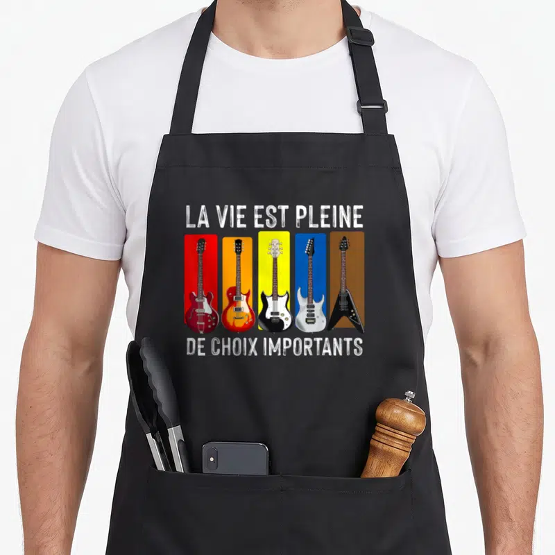 Tablier de cuisine noir avec cinq guitares électriques sur fonds colorés et texte humoristique en blanc.