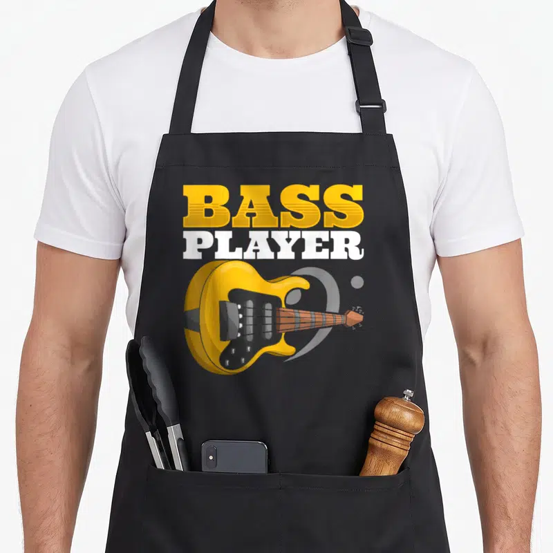 Tablier de cuisine noir avec une basse électrique jaune et l'inscription Bass Player en lettres orange et blanches.