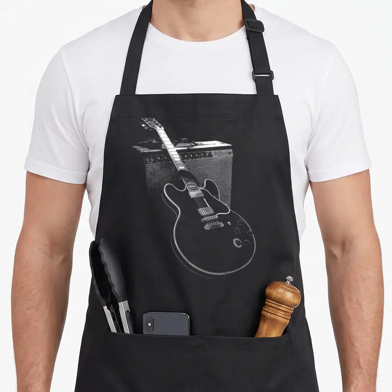 Tablier de cuisine noir avec une guitare électrique et un ampli de blues dessinés en lignes blanches.
