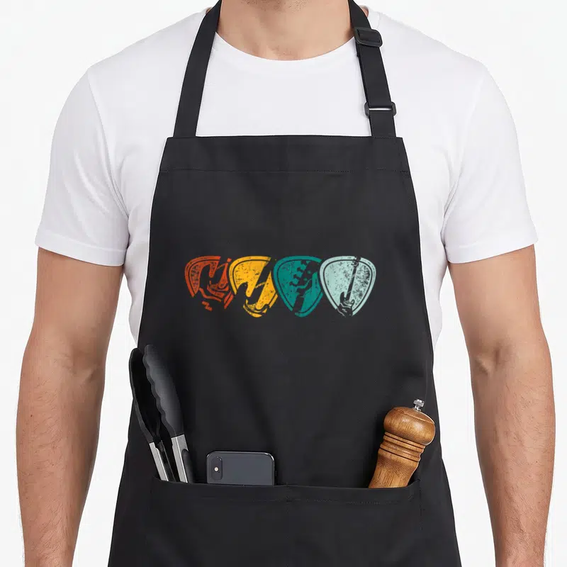 Tablier de cuisine noir avec quatre médiators colorés contenant des silhouettes de basses électriques en style rétro.