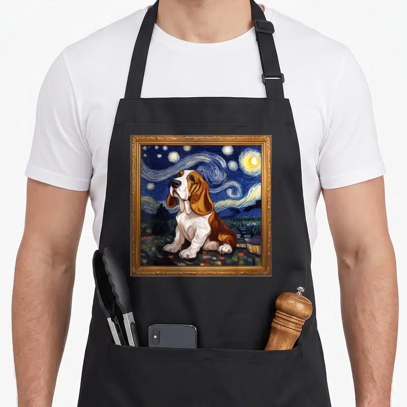 Tablier de cuisine noir avec un Basset Hound assis devant un ciel tourbillonnant évoquant La Nuit étoilée, encadré de doré.