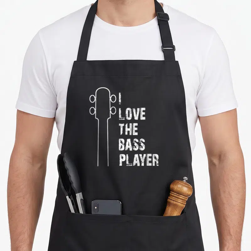 Tablier de cuisine noir avec illustration de tête de guitare et texte I love the bass player en blanc.