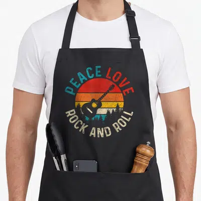 Tablier de cuisine noir avec illustration vintage d'une guitare et texte Peace Love Rock and Roll coloré.