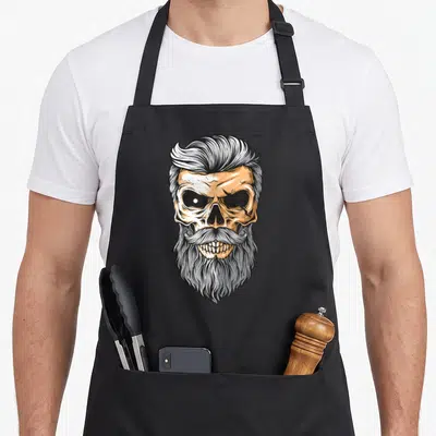 Tablier de cuisine noir avec illustration d'un crâne barbu aux cheveux en coiffure vintage et aux teintes orange et gris.