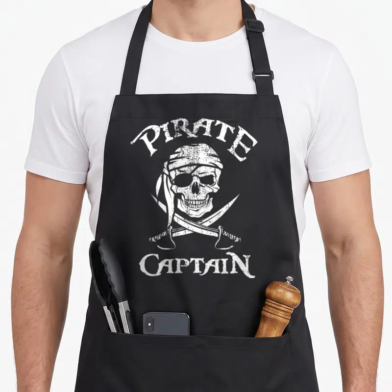 Tablier de cuisine noir avec illustration blanche d'un crâne de capitaine pirate coiffé d'une bandeau et de deux sabres croisés sous le visage.
