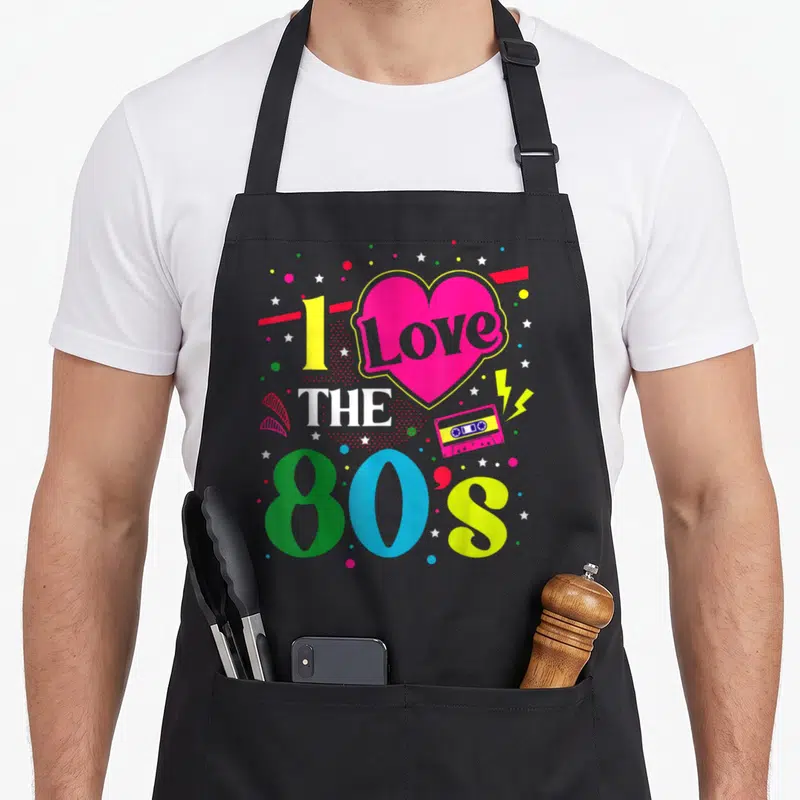 Tablier de cuisine noir avec motif I Love The 80's cœur rose et cassette audio colorée.