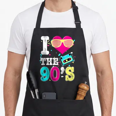 Tablier de cuisine noir avec inscription I Love The 90's, cassette audio rose et lunettes à lamelles jaunes colorées.