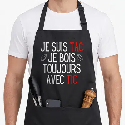 Tablier de cuisine noir avec le texte Je Suis Tac Je Bois Toujours Avec Tic en blanc et rouge.