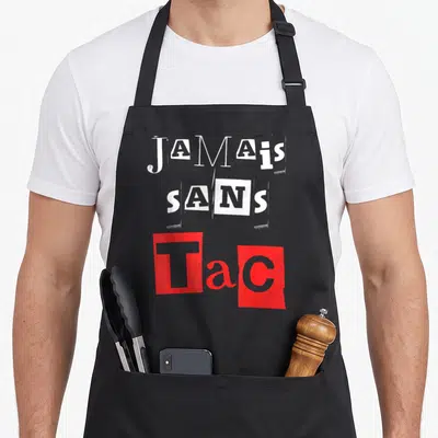 Tablier de cuisine noir avec l'inscription Jamais Sans Tac en blanc et rouge sur fond gris uni.
