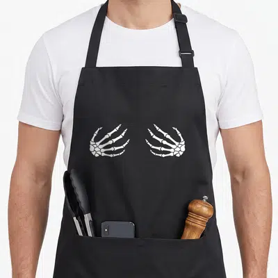 Tablier de cuisine noir avec deux mains squelette blanches dessinées au centre.