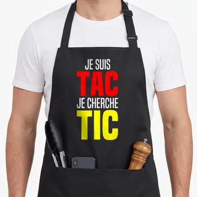 Tablier de cuisine noir avec l'inscription Je suis TAC Je cherche TIC en lettres rouges et jaunes.