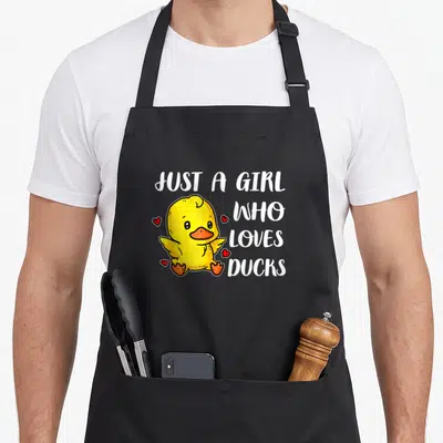 Tablier de cuisine noir avec un canard jaune mignon entouré de petits cœurs rouges et du texte blanc Just A Girl Who Loves Ducks.