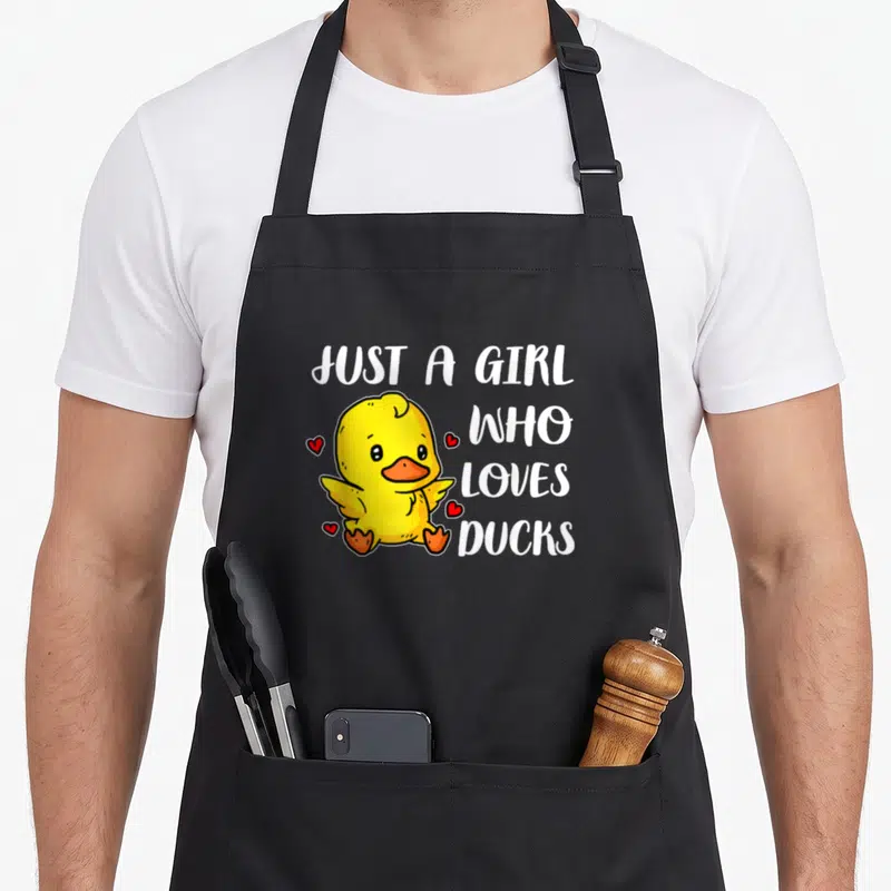 Tablier de cuisine noir avec un canard jaune mignon entouré de petits cœurs rouges et du texte blanc Just A Girl Who Loves Ducks.