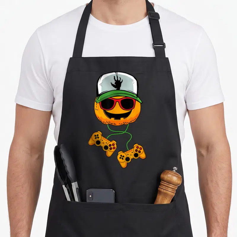 Tablier de cuisine noir avec pumpkin gamer portant des lunettes rouges, une casquette et deux manettes de jeu vidéo oranges.