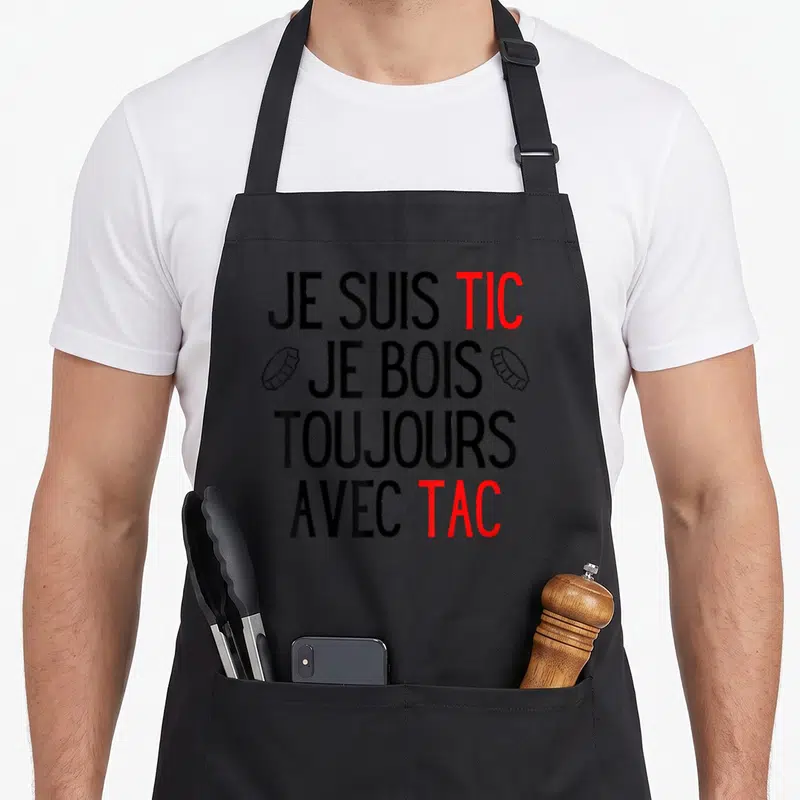 Tablier de cuisine noir avec l'inscription Je suis Tic Je bois toujours avec Tac en noir et rouge, flanquée de deux bouchons de bière.