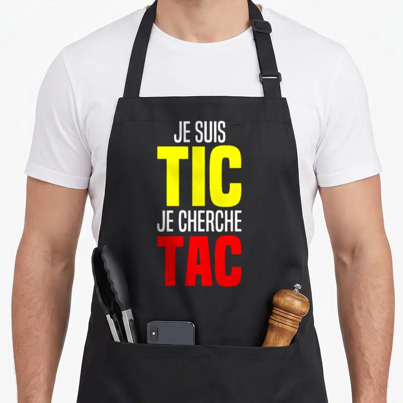 Tablier de cuisine noir avec inscription Je suis TIC Je cherche TAC en jaune et rouge.