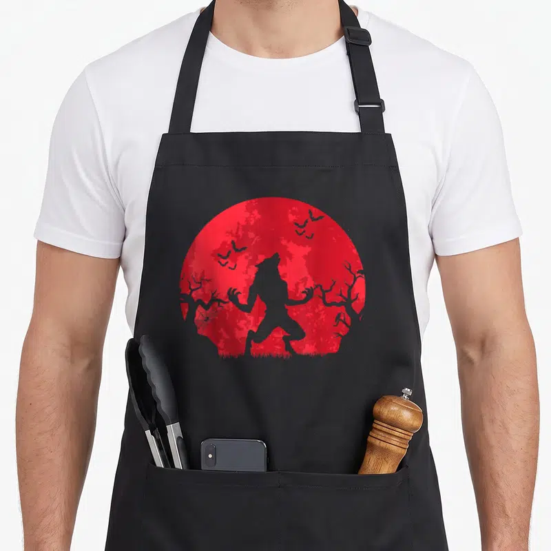 Tablier de cuisine noir avec silhouette loup-garou devant lune rouge sang et chauves-souris volantes.