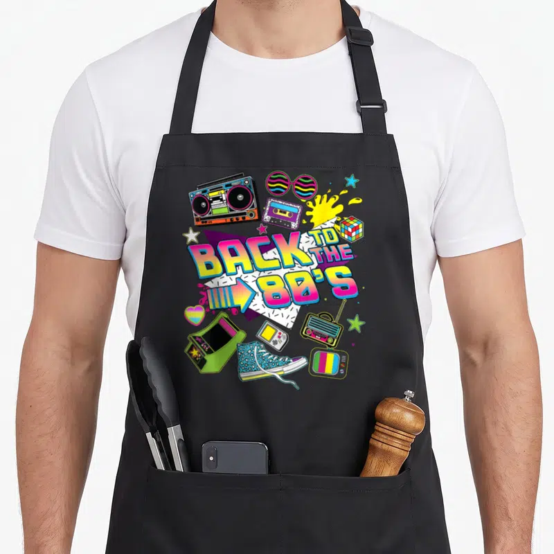 Tablier de cuisine noir avec illustration colorée Back to the 80s incluant une boombox, des lunettes et une console de jeu.