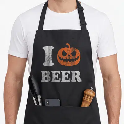 Tablier de cuisine noir avec une citrouille orange et le texte I Love Beer en blanc texturé.