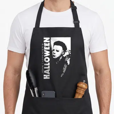 Tablier de cuisine noir avec illustration blanche de Michael Myers et texte vertical Halloween John Carpenter.