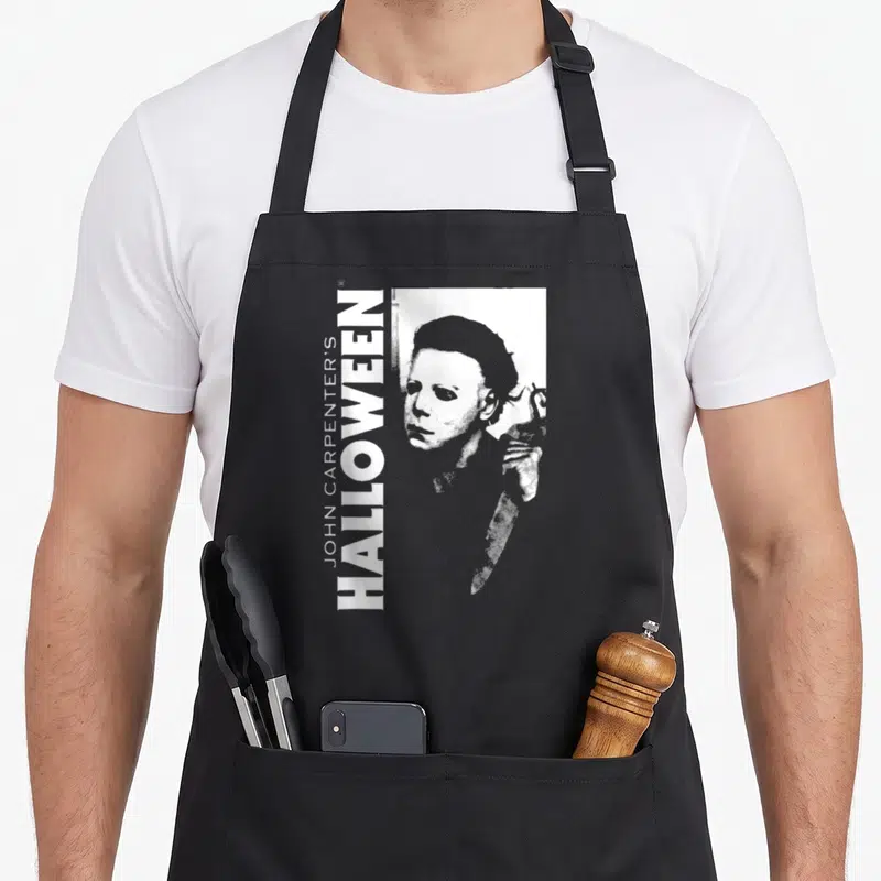 Tablier de cuisine noir avec illustration blanche de Michael Myers et texte vertical Halloween John Carpenter.