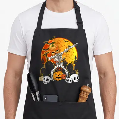 Tablier de cuisine noir avec squelette en train de faire le dab au milieu d'un cimetière et de citrouilles.