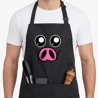 Tablier de cuisine noir avec un visage de cochon rose aux grands yeux expressifs et au nez proéminent.