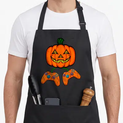 Tablier de cuisine noir avec une citrouille Halloween aux pieds en forme de manettes de jeu vidéo orange.