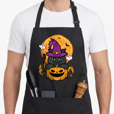 Tablier de cuisine noir avec illustration d'un chat sorcière sur une citrouille orange et des fantômes blancs.