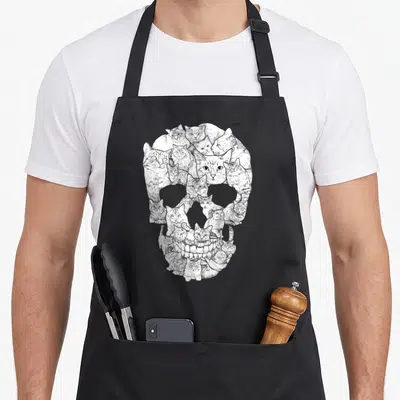 Tablier de cuisine noir avec illustration d'un crâne composé de multiples têtes de chats dessinés en noir et blanc.