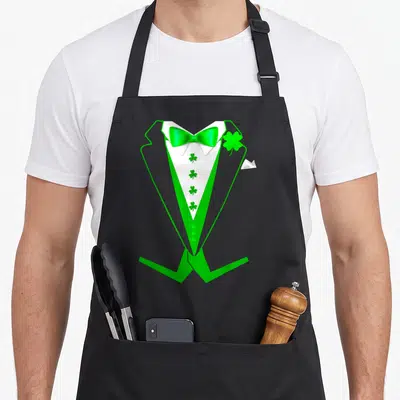 Tablier de cuisine noir avec illustration d'un smoking vert, nœud papillon brillant et trèfles à quatre feuilles sur le gilet blanc.