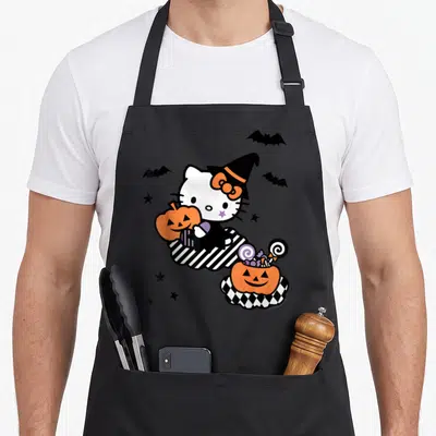 Tablier de cuisine noir avec Hello Kitty Sorcière tenant une citrouille orange et des bonbons colorés sur fond gris uni.