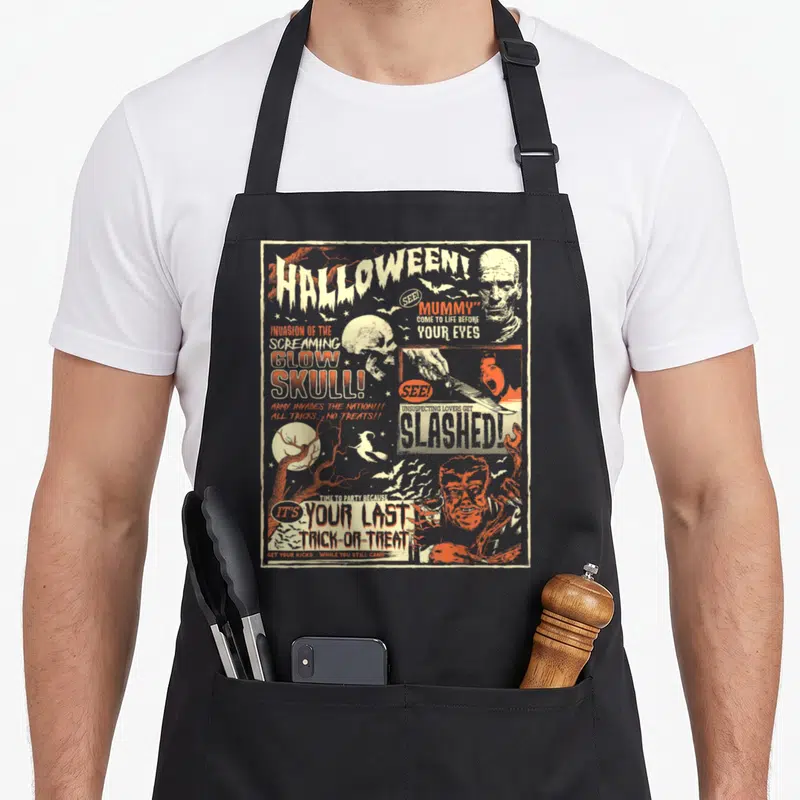 Tablier de cuisine noir avec affiche vintage Halloween montrant un crâne, une momie et des textes comme Slashed et Glow Skull en orange et blanc.