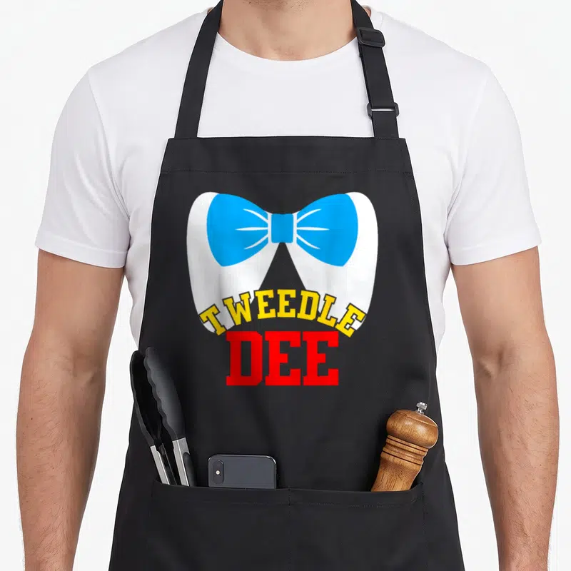 Tablier de cuisine noir avec un grand nœud papillon bleu et le texte Tweedle Dee en lettres jaunes et rouges.