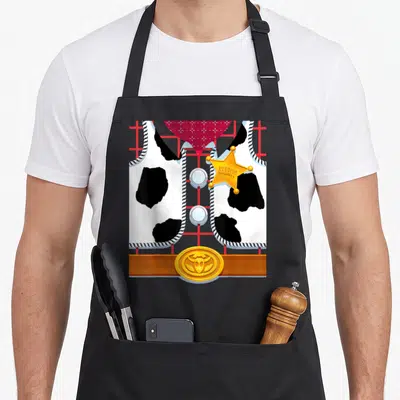 Tablier de cuisine noir avec motif costume de Sheriff Woody, étoile dorée et gilet à pois noirs sur fond quadrillé rouge.