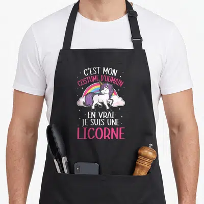 Tablier de cuisine noir avec une licorne blanche, un arc-en-ciel et le texte C'est mon costume d'humain en vrai je suis une licorne.