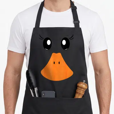 Tablier de cuisine noir avec visage de canard aux grands yeux noirs et bec orange vif.