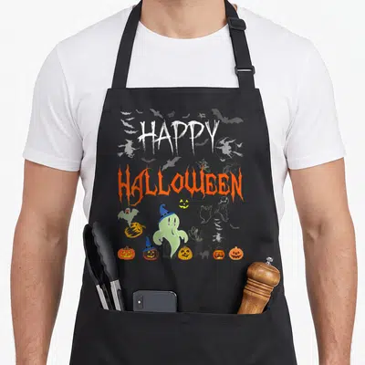 Tablier de cuisine noir avec inscription Happy Halloween et motifs de fantômes, citrouilles et maison hantée.