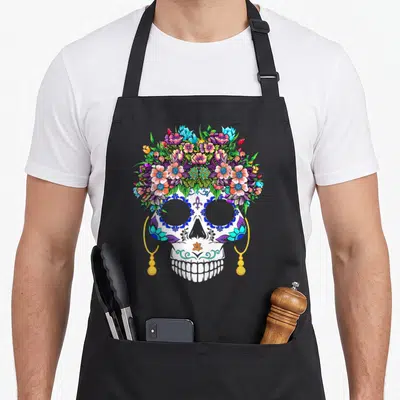 Tablier de cuisine noir avec un crâne décoré de fleurs multicolores et d'oreilles dorées.